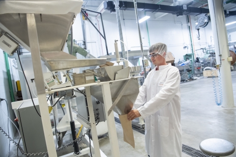 An individual holds a bag at the end of a dispenser to package flour.