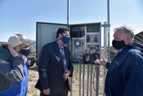 three people look at open electrical box on a sunny day
