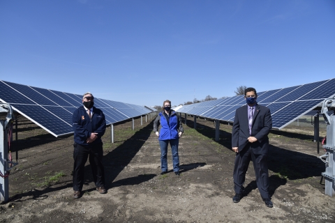 three people pose in front of rows of tracking solar panels