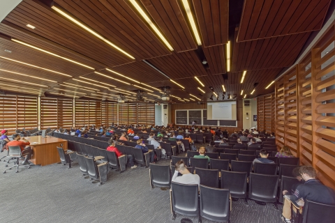 Students sitting in seats taking notes while watching a professor give a lecture.