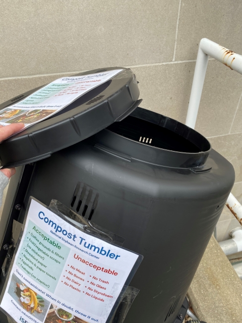 Close view of the compost tumbler with an unscrewed lid. 