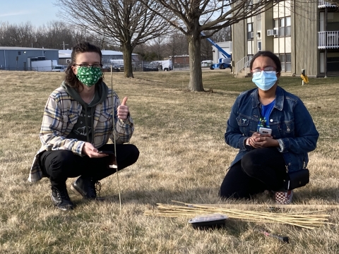 Students in masks kneel by bamboo stakes outside in early spring