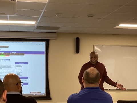man addresses a room with a screen showing the iCAP Portal